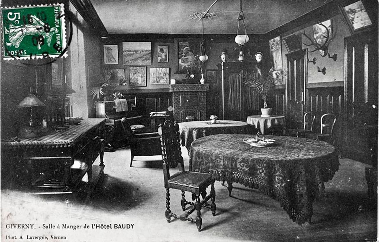 Carte postale timbrée montrant la salle à manger de l’hôtel Baudy, ses tables nappées et ses tableaux accrochés aux murs