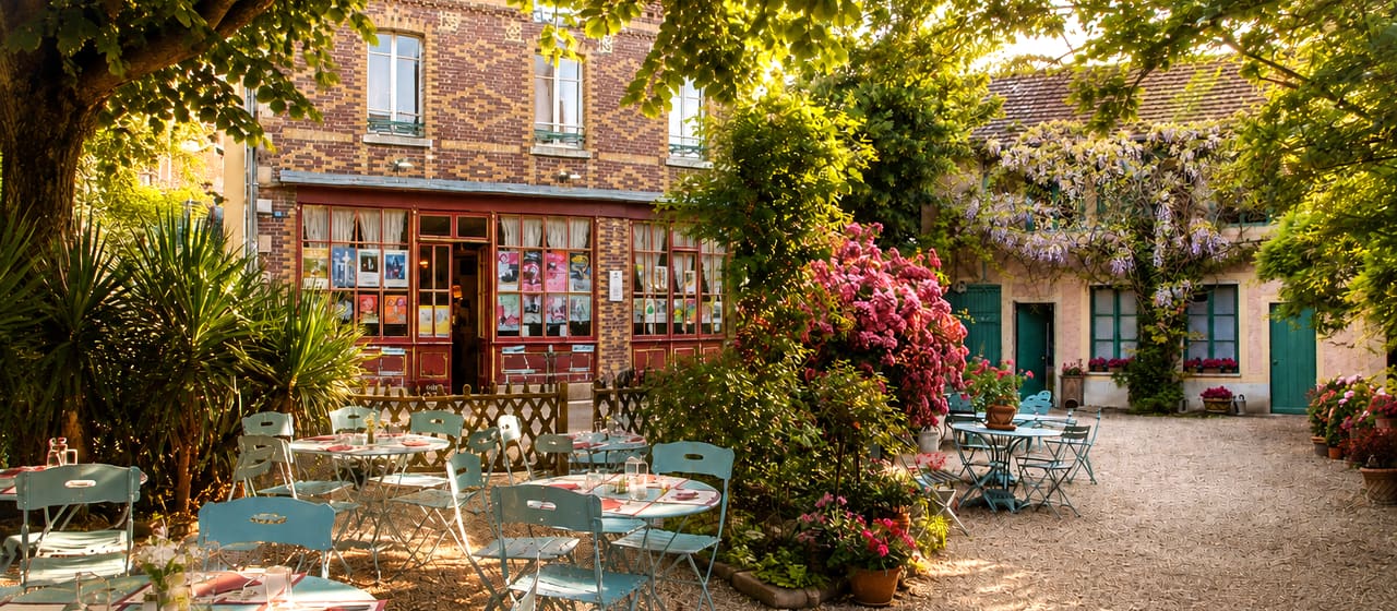 La cour du Restaurant Baudy, ses tables dressées sous les arbres et la glycine en fleurs